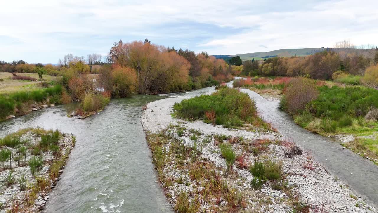 A tranquil river flows through lush greenery and rocky banks under a bright sky at Lake Tekapo, New Zealand