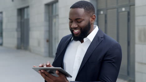 afro businessman typing message on tablet at street. worker using pad outdoors