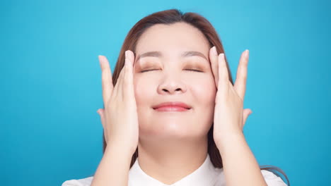 파란색 배경-3의 웰빙 피부 관리를 위해 노화 방지 밤 크림으로 얼굴을 부드럽게 문지르는 완벽하고 예쁜 아시아 여성