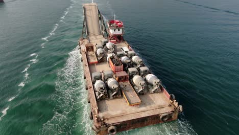 Barge-loaded-with-Concrete-mixer-trucks-pulled-to-port-by-a-Tugboat-in-Hong-Kong-bay,-Aerial-view