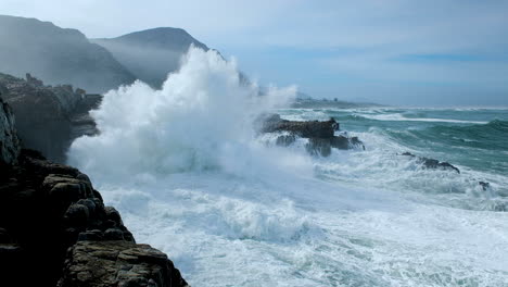 huge wave making a big splash as it crashes into rocks on rocky coastline, hermanus