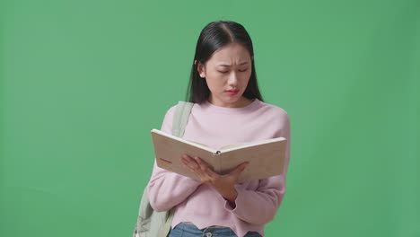 upset asian woman student reading a book in green screen studio