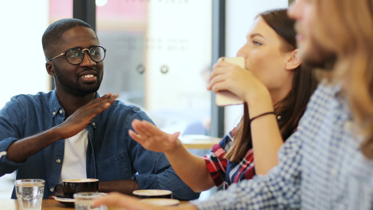 vista cercana de un grupo multiétnico de amigos sonriendo y haciendo gestos divertidos sentados en una mesa en un café