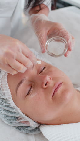 cosmetologist applying moisturizing peeling acid on skin around eyes of woman antiaging treatment