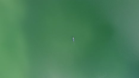 Aerial-view-of-people-row-a-wooden-boat-in-turquoise-blue-lake-or-sea