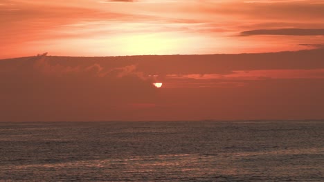 Calm-sea-at-sunset,-with-the-sun-at-low-orange-sky-with-beautiful-clouds