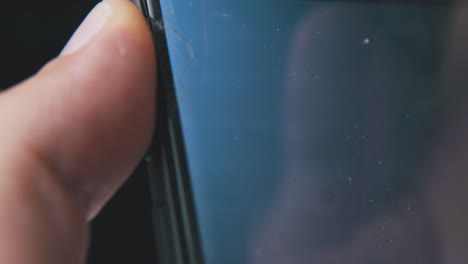 man-checks-broken-phone-on-black-background-extreme-closeup
