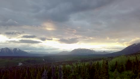 Sensational-countryside-scenic-Yukon-flight-above-green-lush-tree-forest-and-vegetation-with-mountain-range-in-background-on-dramatic-sunny-day-and-sunset,-Canada,-overhead-aerial-rising