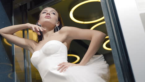 mujer elegante en un vestido blanco posando por un ascensor