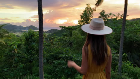mujeres jóvenes con vestido amarillo y sombrero viendo la puesta de sol dorada a través de los árboles de la selva en lombok, indonesia