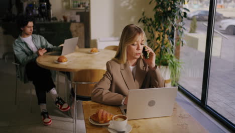 woman working on laptop and talking on phone in a coffee shop