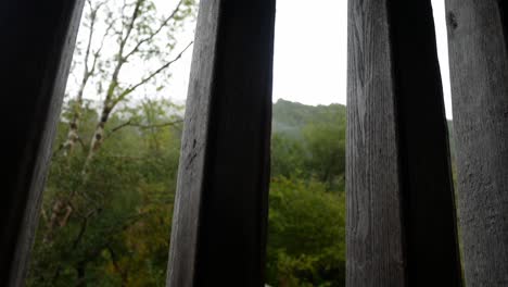 raining weather in rural mountain countryside through rustic oak wood barn beams window dolly right looking up