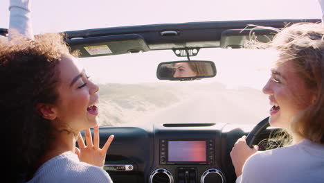 Dos-Mujeres-Jóvenes-Felices-Conduciendo-Con-El-Techo-Corredizo-Abierto