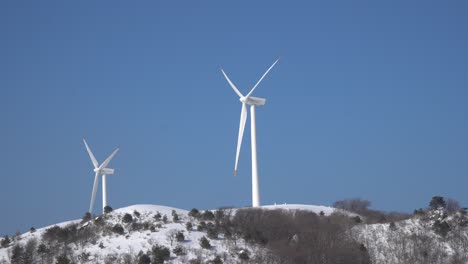 Dos-Molinos-De-Viento-Se-Mueven-Con-Fuerza-Para-Generar-Electricidad-En-La-Montaña-Cubierta-De-Nieve,-Corea-Del-Sur