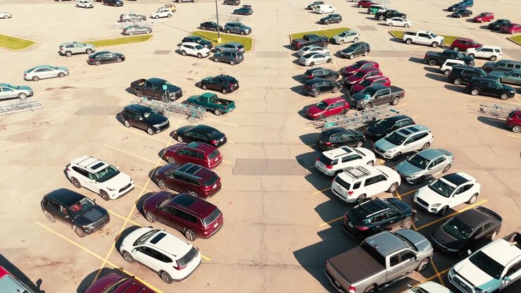 Acercamiento angular con dron sobre un gran estacionamiento con coches aparcados en filas ordenadas, mostrando el diseño y la distribución urbana.