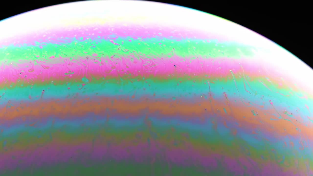 Close-up view of colorful striped patterns on a soap bubble under dark lighting.