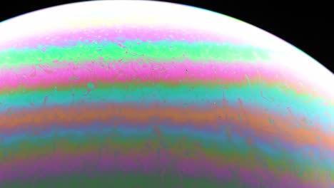 close-up view of colorful striped patterns on a soap bubble under dark lighting.