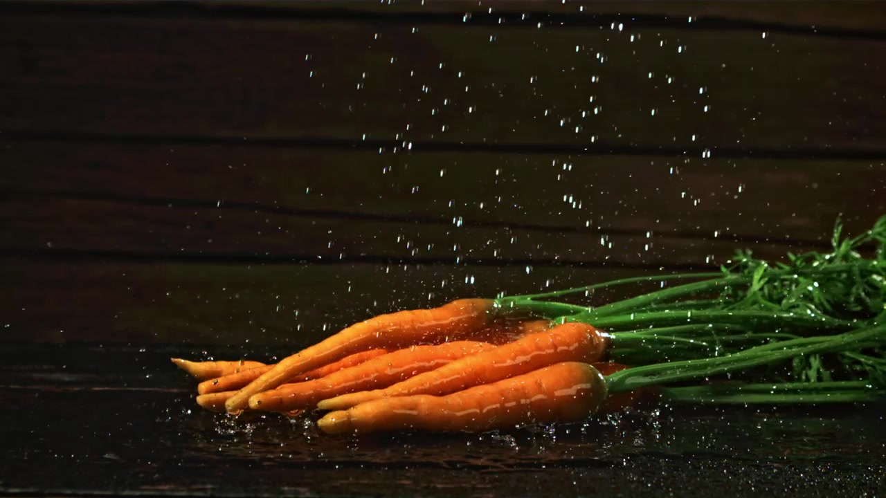Gocce d'acqua che cadono su carote fresche al rallentatore