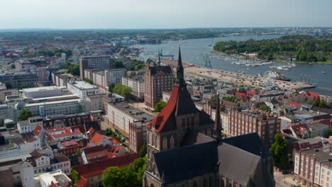 Backwards-reveal-of-brick-gothic-style-Saint-Marys-church.-Panoramic-aerial-view-of-city-lying-on-bank-of-wide-river
