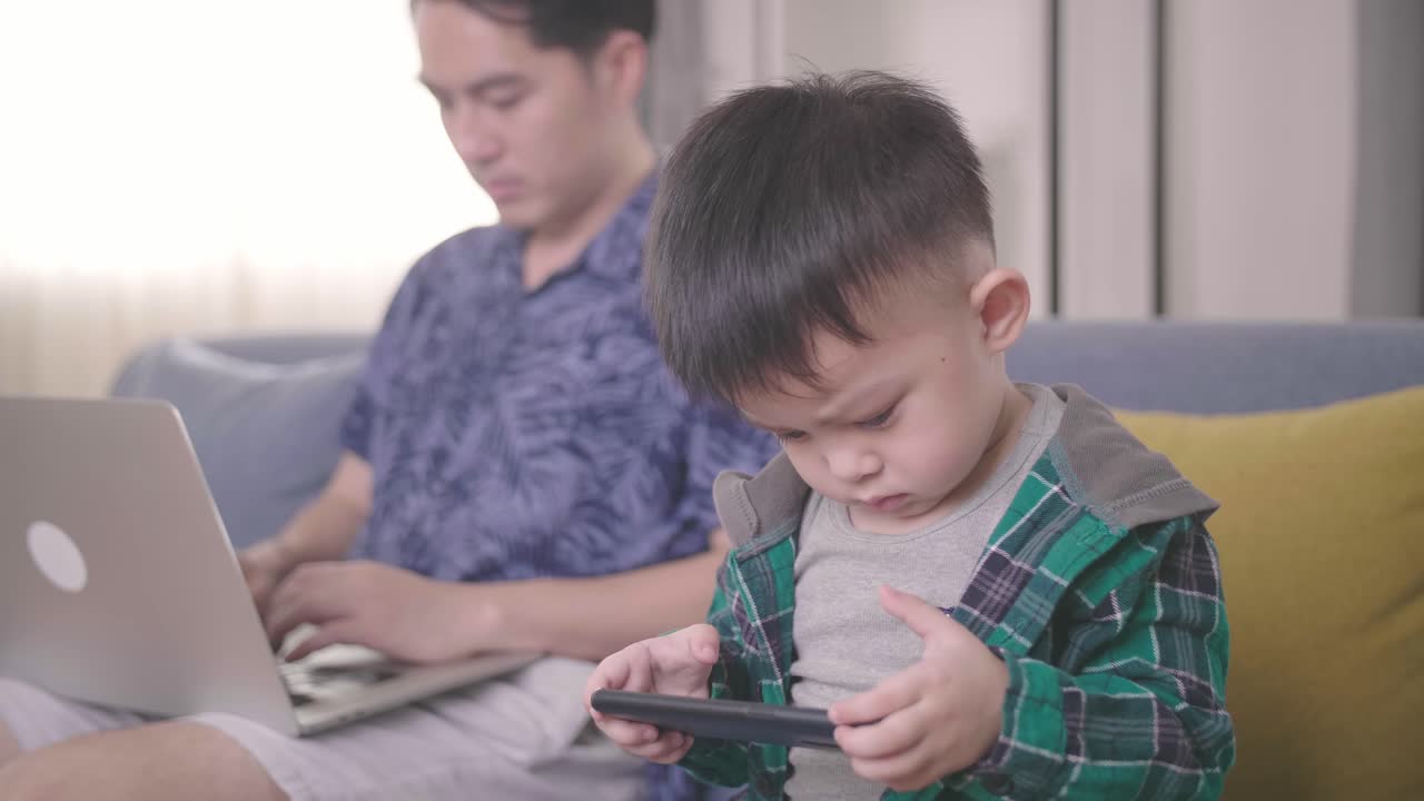 Boring Boy Using Smartphone While Father Working On Laptop