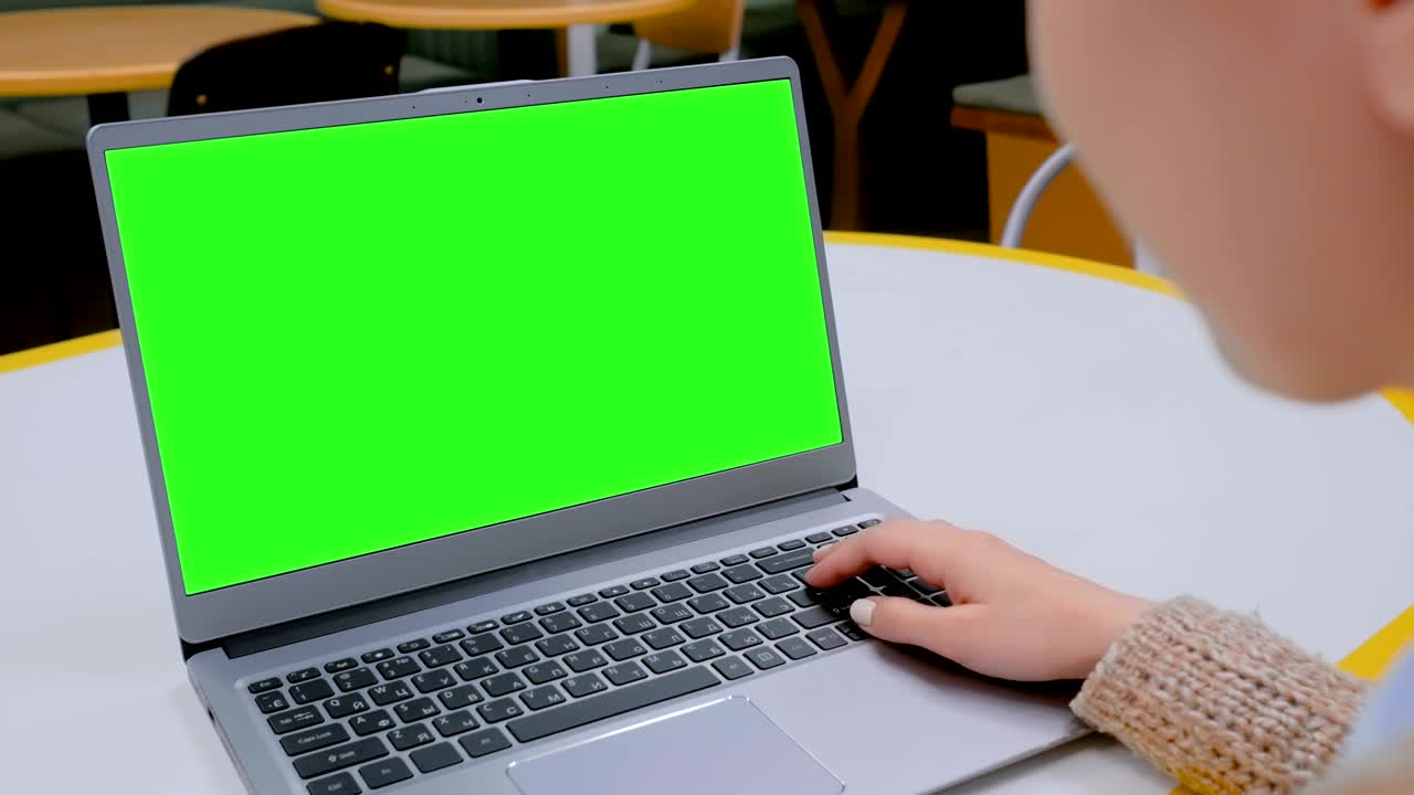 mujer mirando una computadora portátil con una pantalla verde en blanco en un café
