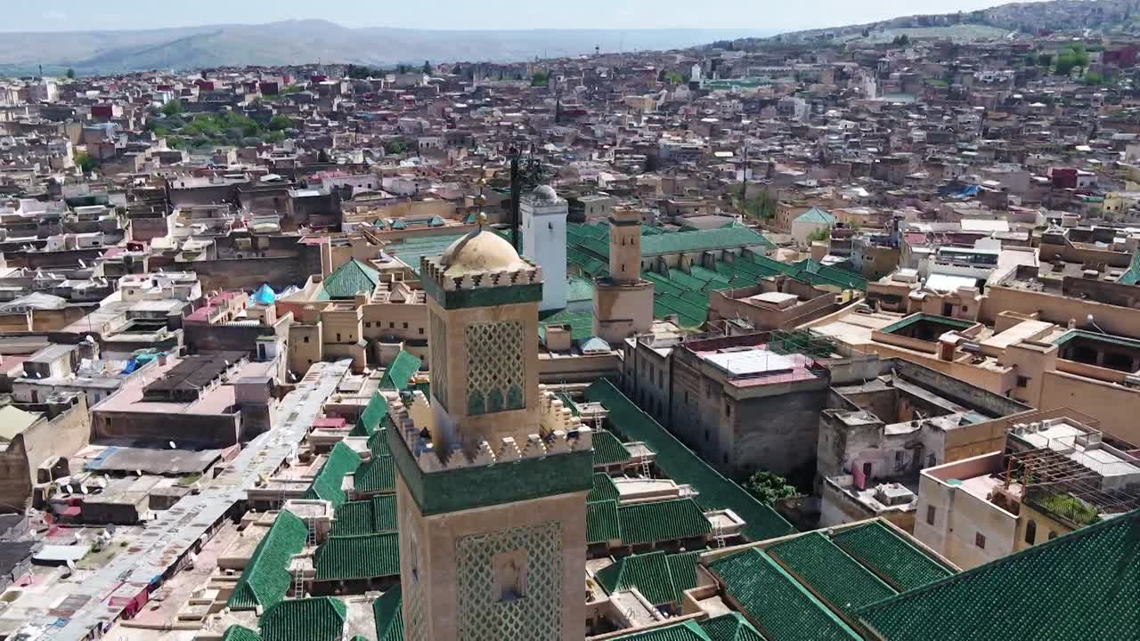 Tarihi Al-Qarawiyyin üniversitesi minaresinin odaklanmış drone çekimi. İkonik yeşil çinili çatılar ve Fez'in yoğun antik medina manzarasını sergiliyor; burası dünyanın en eski üniversitesine ev sahipliği yapıyor.