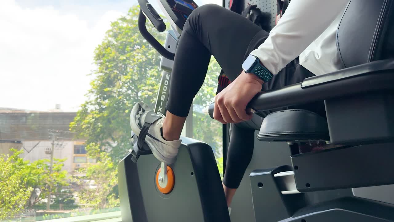 A person exercises on a magnetic recumbent bike indoors, with natural light and greenery visible outside