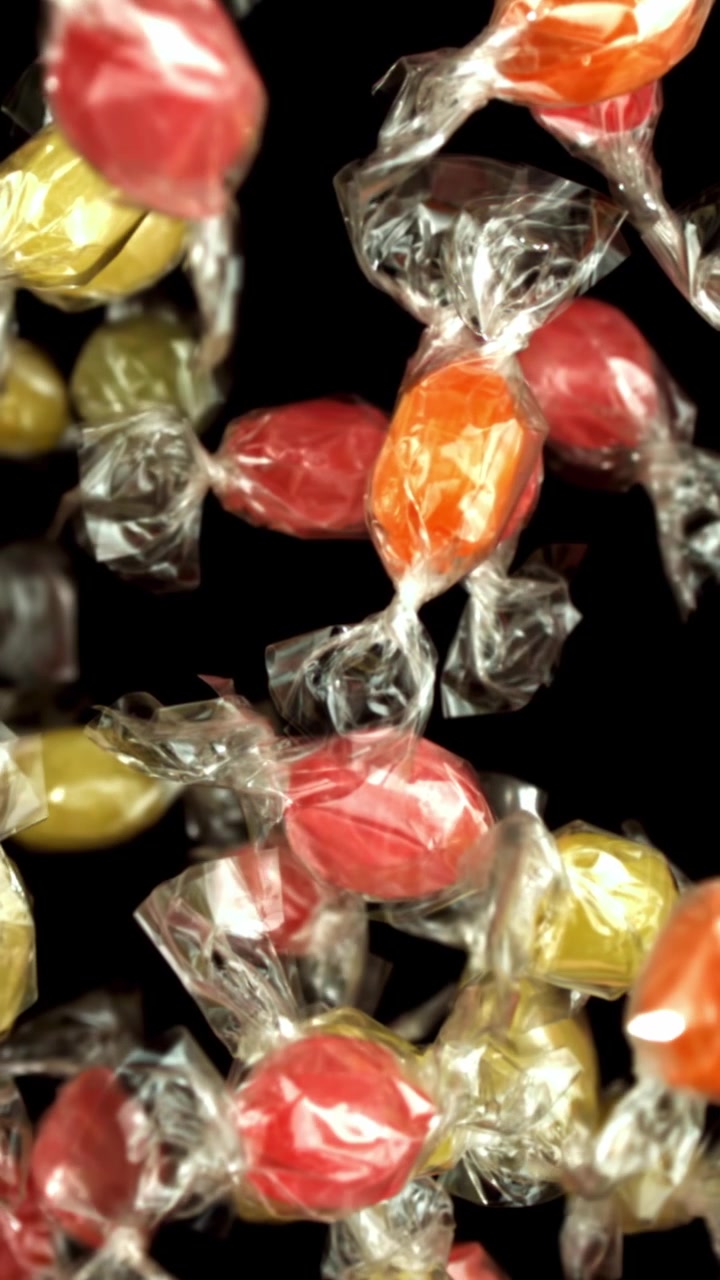 Caramelle colorate incartate che cadono al rallentatore su sfondo nero