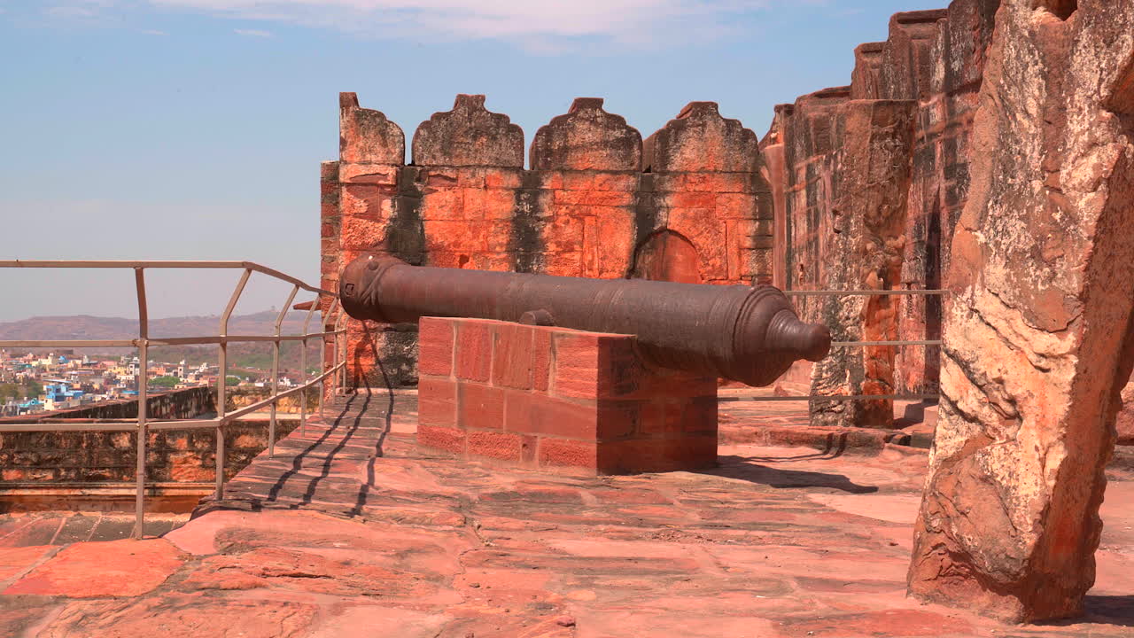 En statisk optagelse af en historisk jernkanon monteret på en stenpiedestal langs forsvarsmurene på Mehrangarh Fort, med udsigt over byen Jodhpur, Rajasthan, Indien.