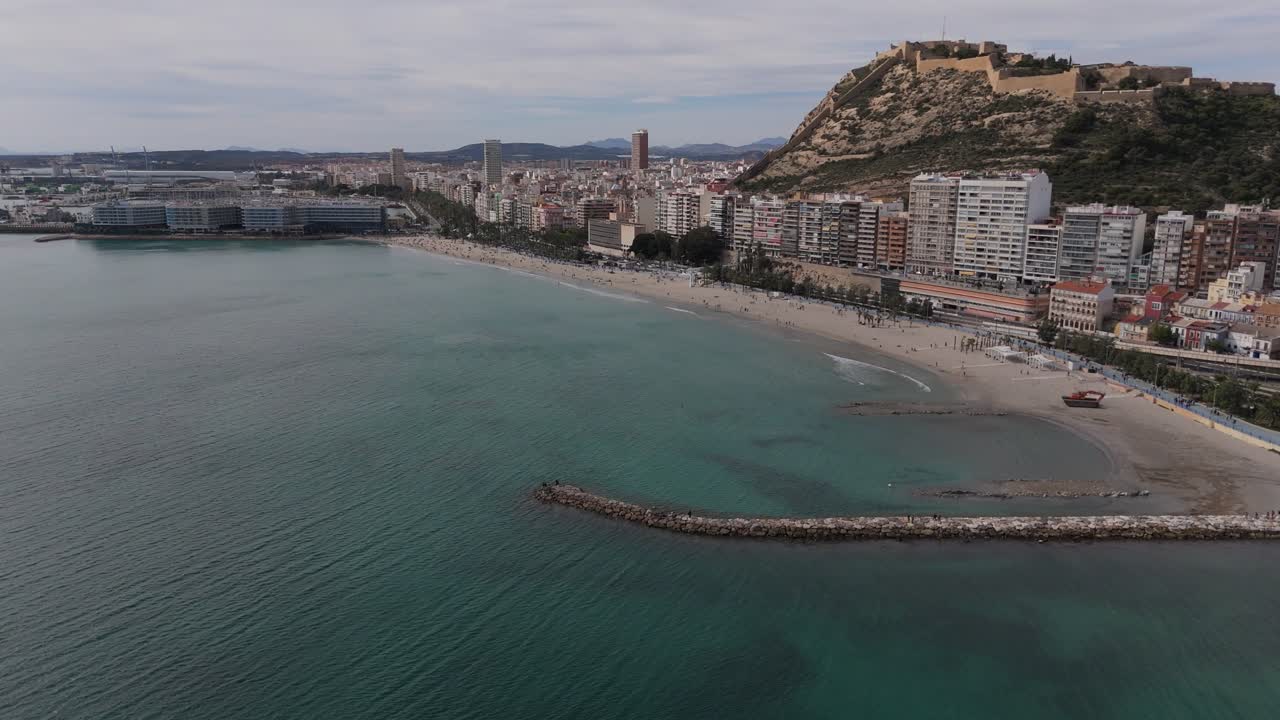 Riprese drone della costa di Alicante con Playa del Postiguet e il Castello di Santa Bárbara sul Monte Benacantil. Il litorale mediterraneo e lo skyline cittadino creano una luminosa scena costiera in Spagna