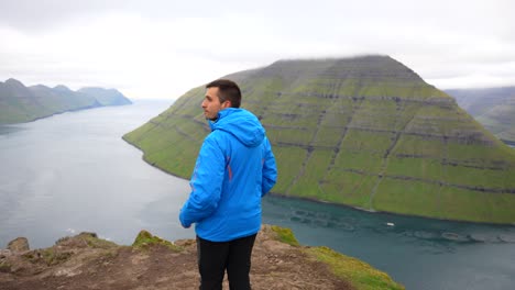 Hombre-Disfrutando-De-La-Vista-Del-Paisaje-Del-Fiordo-Desde-La-Cima-De-La-Montaña-Klakkur,-Islas-Feroe