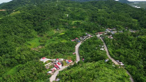 aerial orbit of quaint hillside barangay town with lush tropical greenery and winding roads - buenavista, catanduanes, philippines