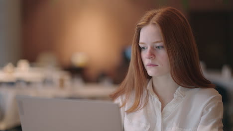 young red-haired female professional writing an important email from her home. modern living room. remote working. serious woman search for inspiration make decision feel lack of ideas