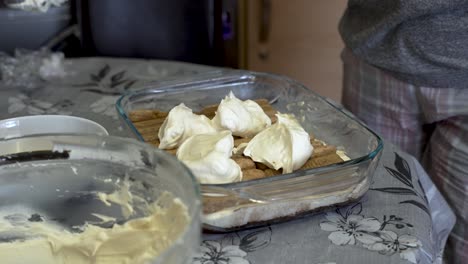 Whipped-Cream-Being-Applied-To-Ladyfingers-By-Spatula-In-Glass-Baking-Tray