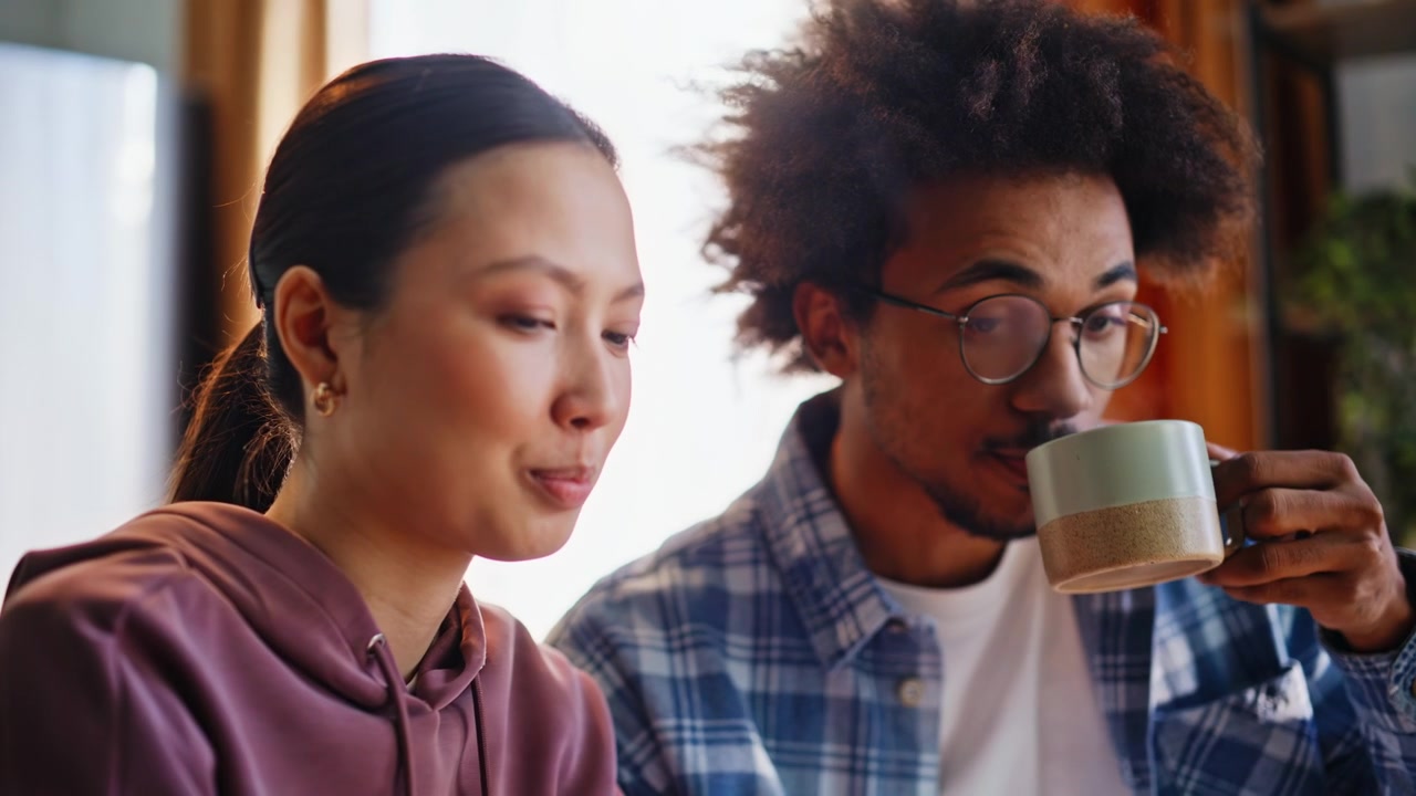 Pareja multiétnica usando el teléfono en casa. Primer plano de hombre bebiendo café