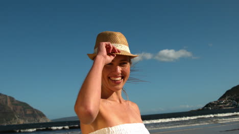 rubia sonriente quitándose el sombrero de sol en la playa