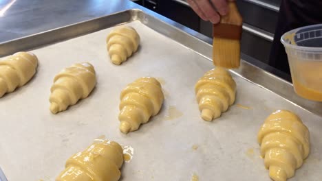 a baker painting egg wash on to croissants that will be baked in a cafe