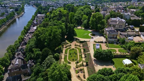 High drone advances toward Jardin de la Perrine in Laval, showing rose garden, Mayenne River, and urban backdrop - France