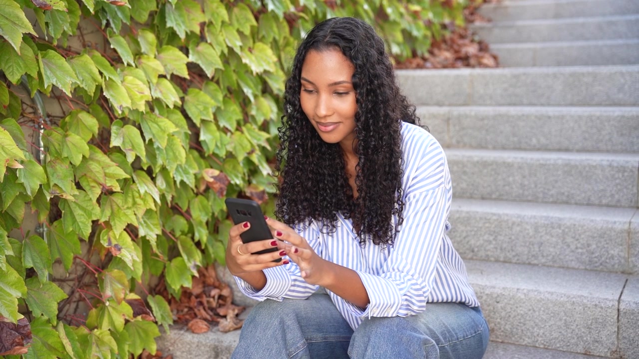 A young woman is using her smartphone while sitting on steps surrounded by vibrant greenery