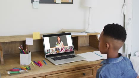 Schoolboy-using-laptop-for-online-lesson-at-home,-with-diverse-teacher-and-class-on-screen