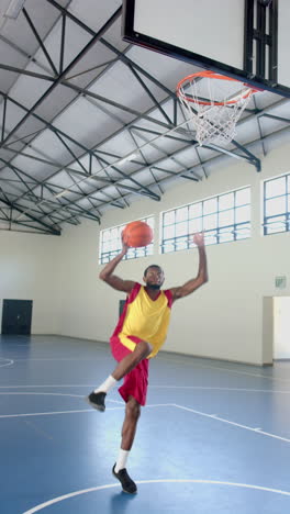 vertical video: playing basketball, man in sportswear shooting ball towards hoop in gymnasium