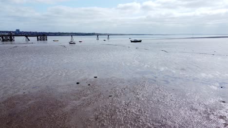 Small-fishing-boat-aerial-push-in-view-of-stranded-vessel-on-muddy-low-tide-on-Liverpool-coastline