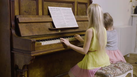 Vista-Lateral-De-Dos-Niñas-Pequeñas-Tocando-El-Piano-Antiguo-En-Casa