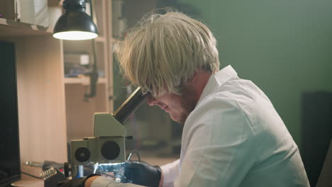 una vista de cerca de un técnico con una peluca rubia intensamente enfocado en un microscopio en un entorno de laboratorio