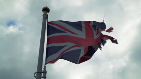 torn union jack flag blowing in strong wind against clouds in slow motion