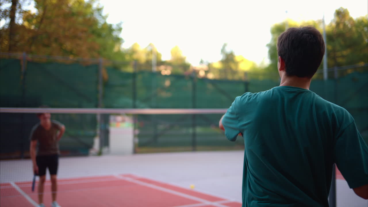 Boys playing pickleball with yellow ball and blue paddle at a court
