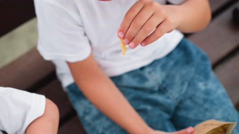 un primer plano de un niño alcanzando un paquete de chips para agarrar un chip, con una vista parcial de la mano de otro niño visible a la derecha
