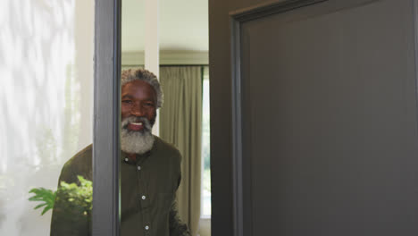 uomo afroamericano anziano che apre una porta d'ingresso e guarda la telecamera