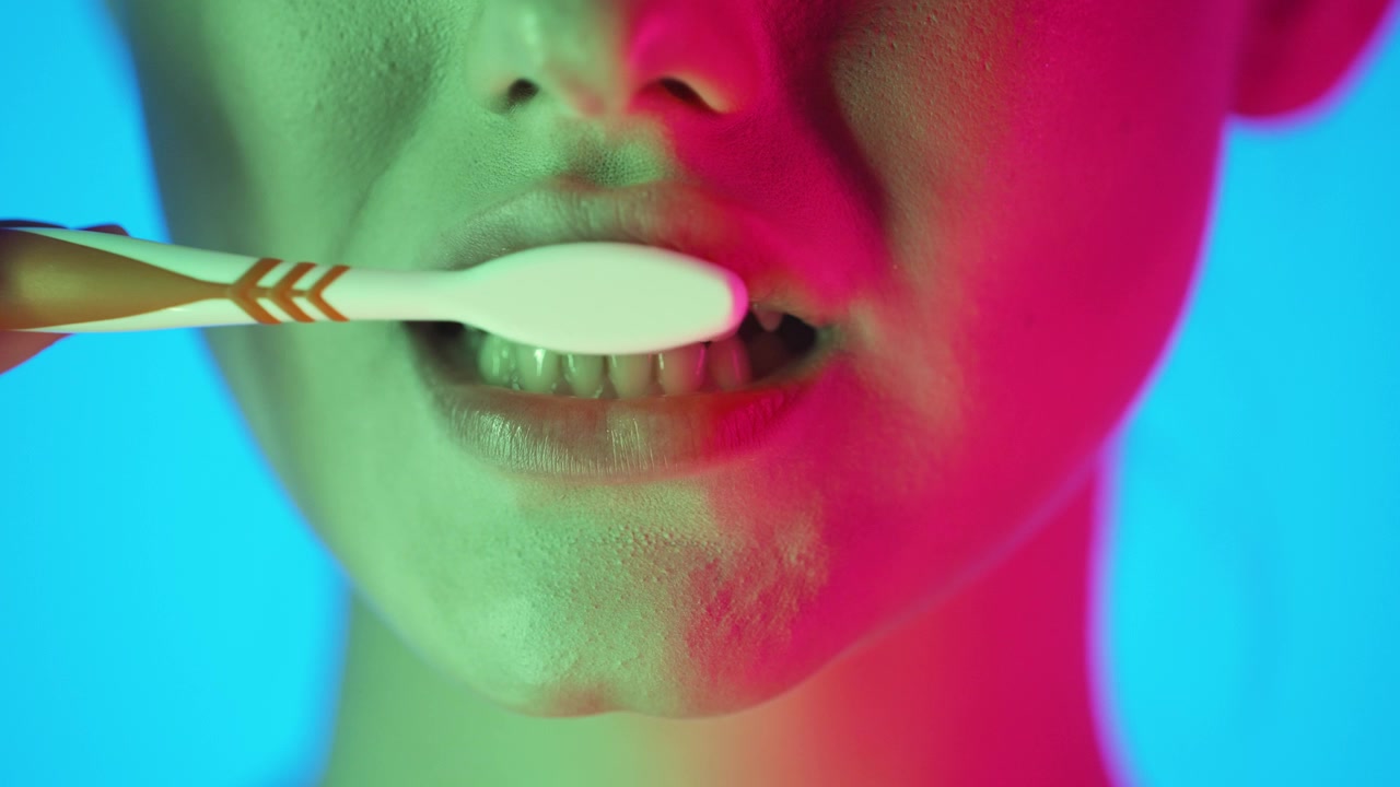 Close-Up Of Woman's Mouth Brushing Teeth With Toothbrush, Colorful Studio Lighting