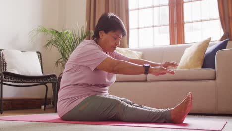 Asian-senior-woman-performing-stretching-exercise-sitting-on-the-yoga-mat-at-home